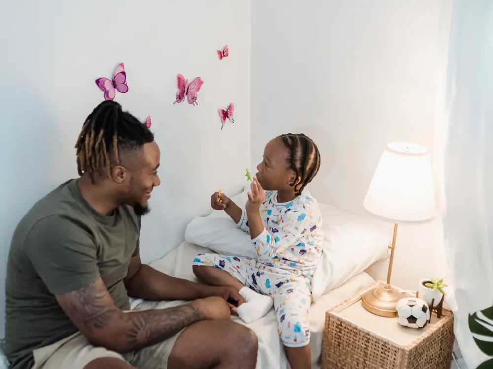 A father and young daughter sharing a warm conversation in a cozy bedroom
