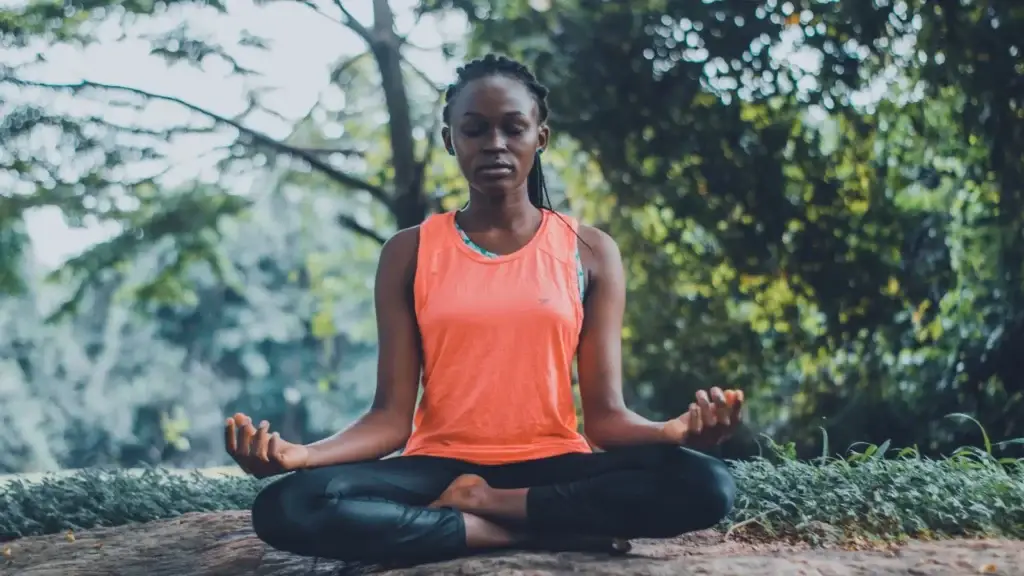 A woman meditating on a tree branch in a peaceful wooded setting